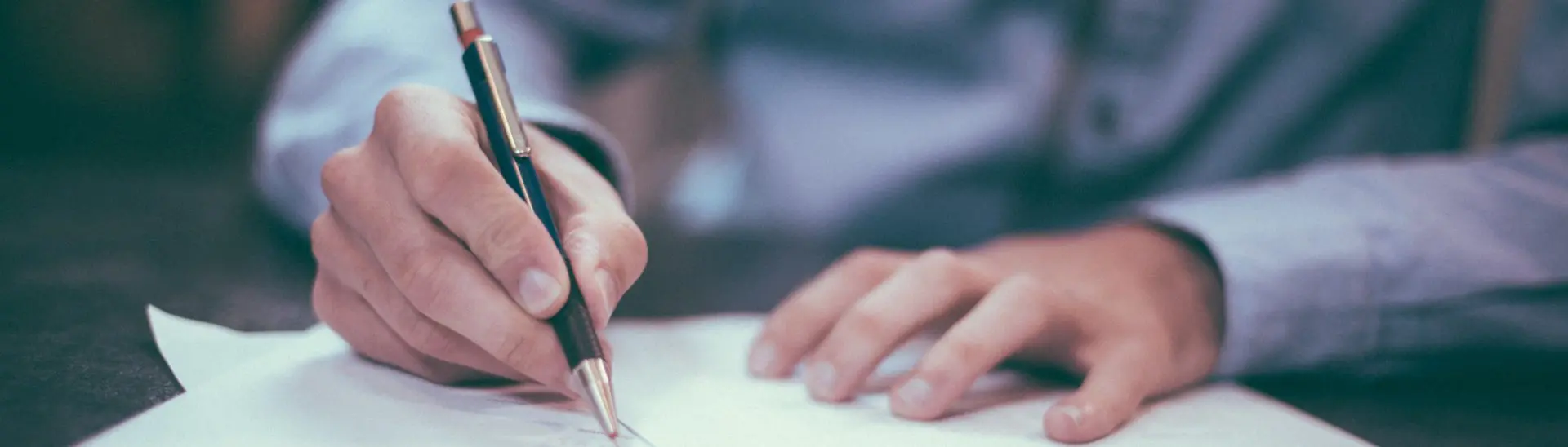 Hands of person in blue button up shirt signing paperwork
